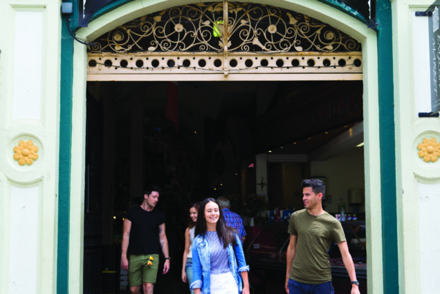 People exiting the ornate entrance of the English Market in Cork, featuring decorative black and gold signboard.